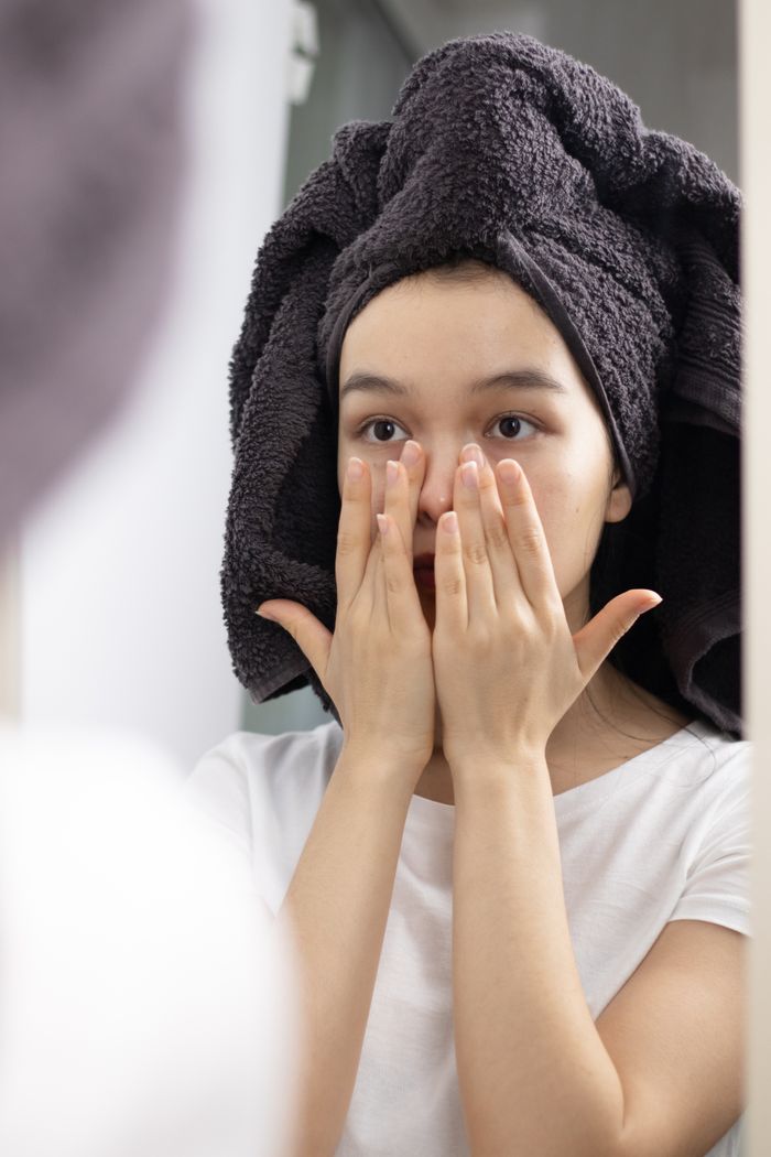 heros-img Close-up of a woman patting her face in the mirror, promoting skincare and relaxation at home.